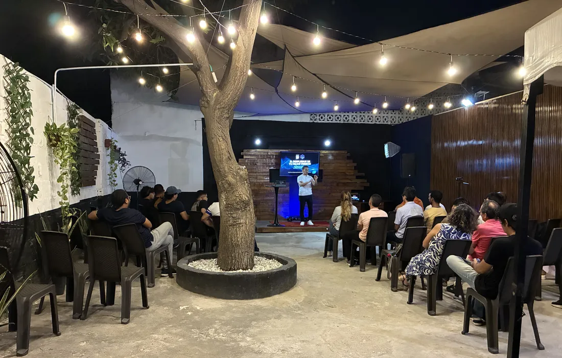 La comunidad de Iglesia Camino reunida al aire libre, bajo luces y alrededor de un árbol, escuchando la predicación
